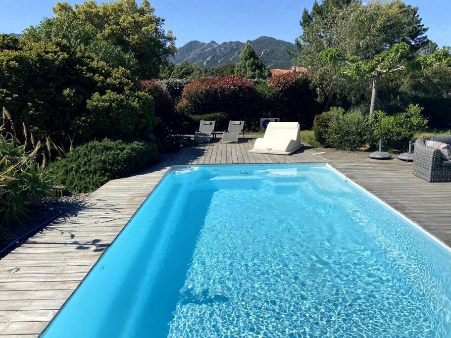 une piscine bleue avec une terrasse en bois et des montagnes dans l'établissement Maison entre mer et montagne, à Lecci