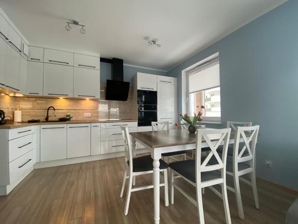 kuchnia z białymi szafkami oraz drewnianym stołem i krzesłami w obiekcie Apartament Rakownica w Jeleniej Górze