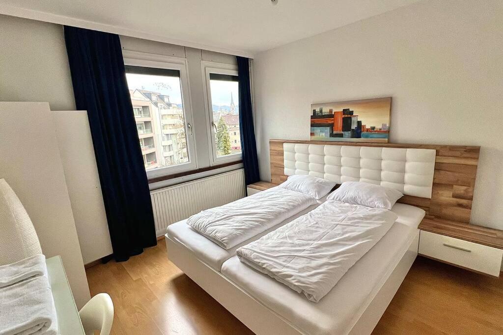 Schlafzimmer mit einem weißen Bett und einem großen Fenster in der Unterkunft Apartment 14 im Herzen von Linz in Linz