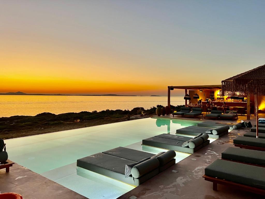 Akre Hotel في ناكسوس تشورا: حمام سباحة مع كراسي للاستلقاء والمحيط عند غروب الشمس