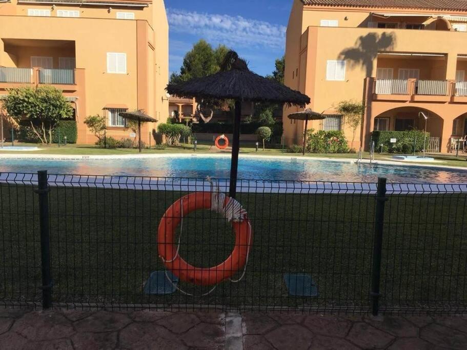 a swimming pool with an umbrella next to a fence at Adosado en Novo Atlantico Golf in Novo Sancti Petri