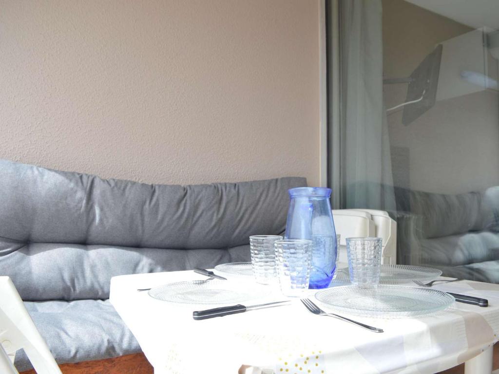 une table blanche avec des verres et un vase bleu sur elle dans l'établissement Appartement T2 avec Piscine, 4 Couchages, Proche Plage - Narbonne Plage - FR-1-229B-97, à Narbonne