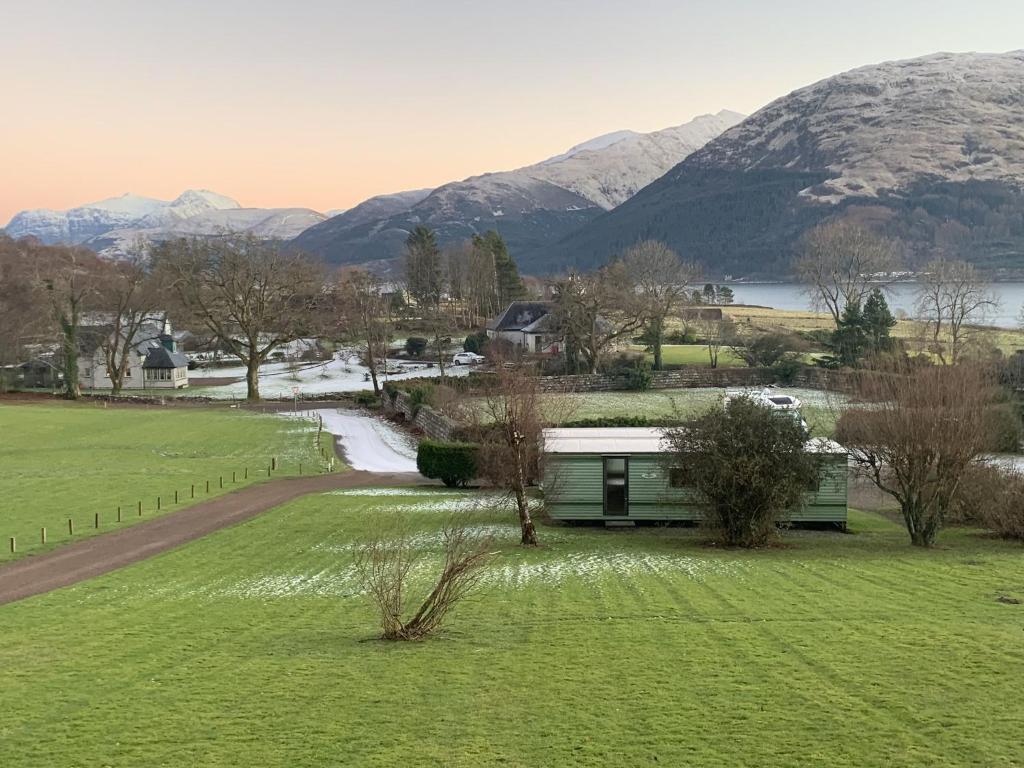 a green building in a field with mountains in the background at Osprey Caravan in Onich