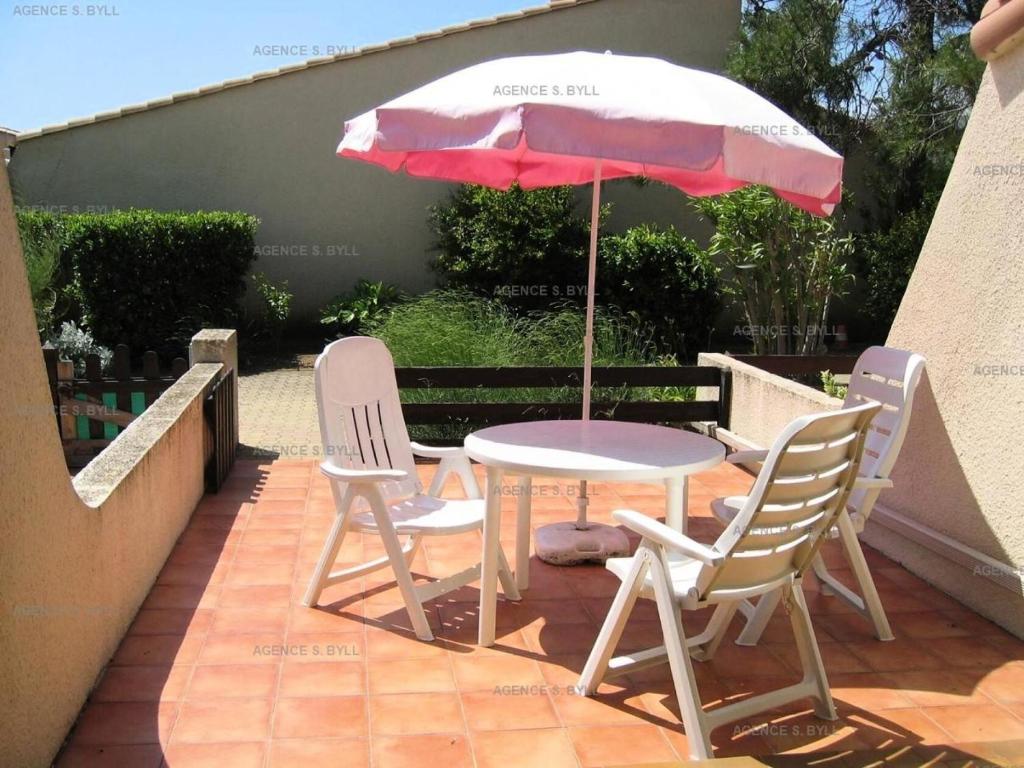 een tafel en stoelen en een parasol op een patio bij Résidence Héliovillage - Maisons & Villas pour 4 Personnes 944 - Naturiste in Cap d'Agde