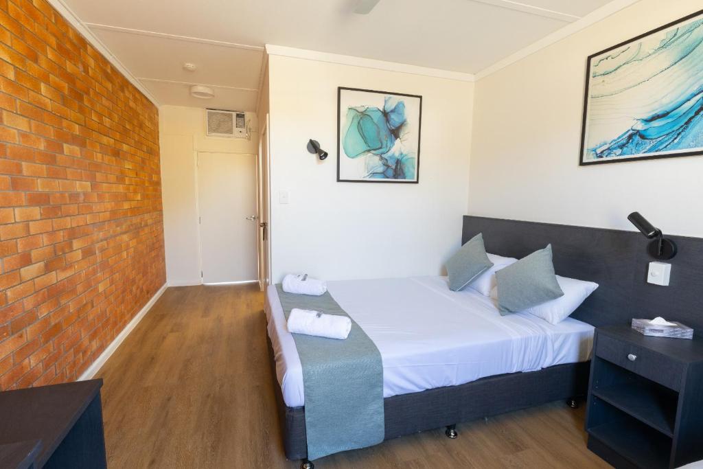 1 dormitorio con cama y pared de ladrillo en The Club Hotel, en Gladstone