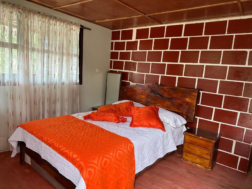 um quarto com uma cama com lençóis laranja e uma parede de tijolos em sol solegüa em Cajamarca
