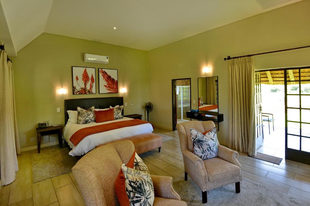 a bedroom with a large bed and two chairs at African Hills Safari Lodge & Spa in Magaliesburg