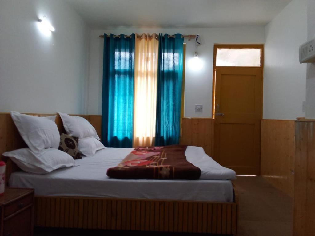 a bedroom with a large bed with blue curtains at iSaint's Kuteer in Manāli