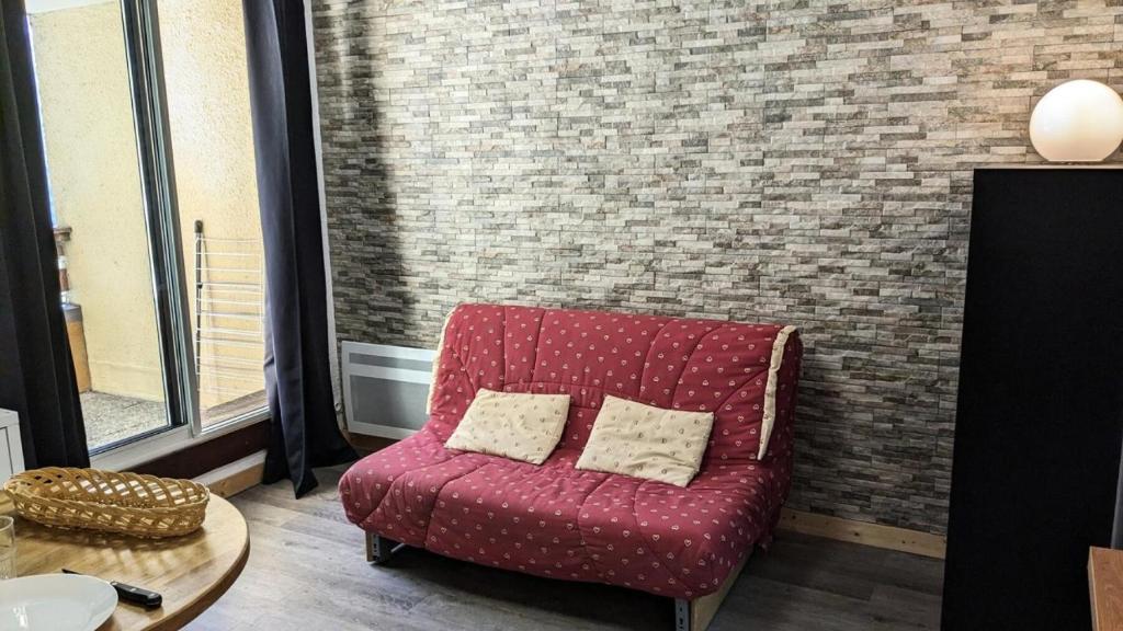 un fauteuil rouge avec deux oreillers assis à côté d'un mur en briques dans l'établissement Résidence Rond-point-pistes Ii - Mini studio 4 pers N° 48B au rond point des pistes avec WIFI MAE-7394, à Orcières