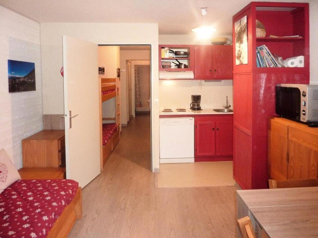 a room with a kitchen with red cabinets and a room with a table at Résidence LE PERESCUELLE - 2 Pièces pour 6 Personnes 664 in Les Orres