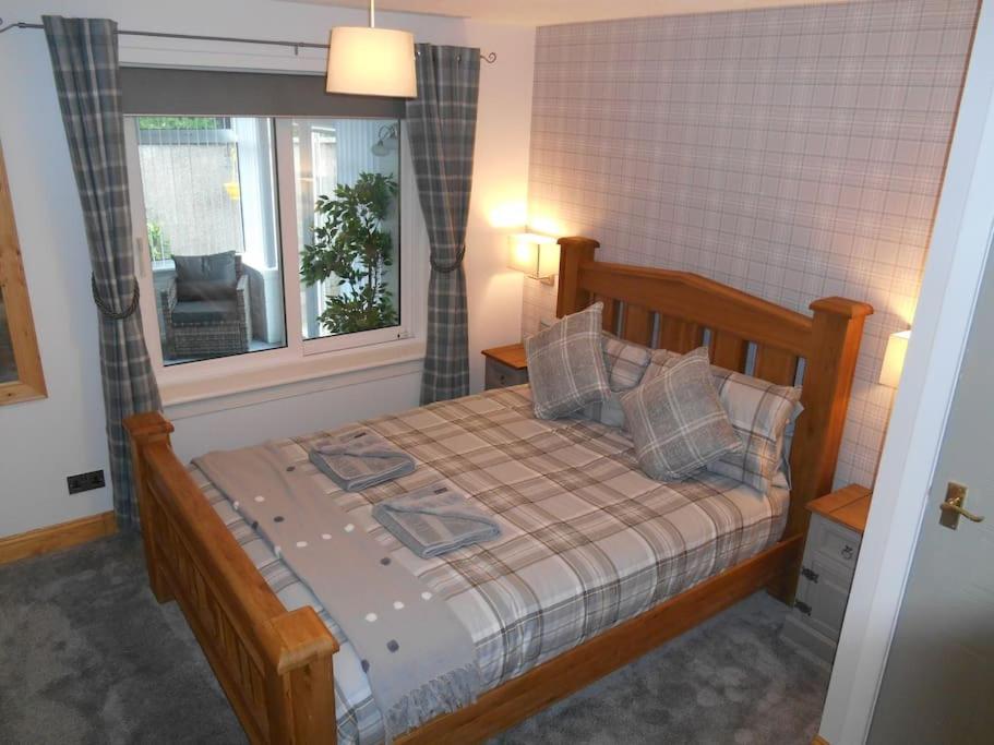 1 dormitorio con cama de madera y ventana en Eliburn Woodside Lodge, en Livingston