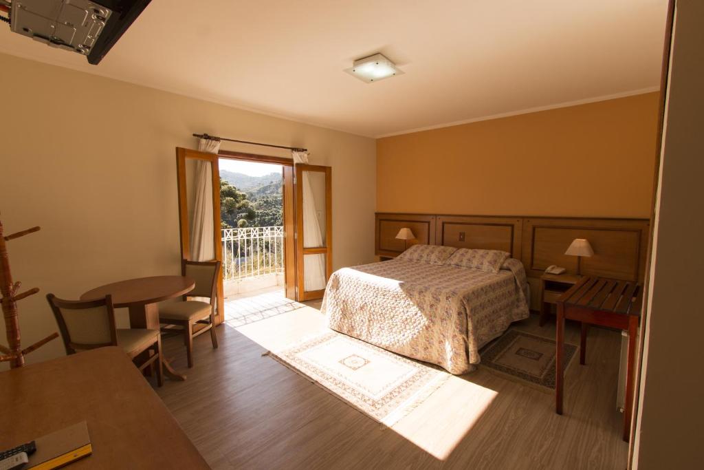 a bedroom with a bed, desk, chair and a lamp at Pousada Alto D'ouro in Campos do Jordão
