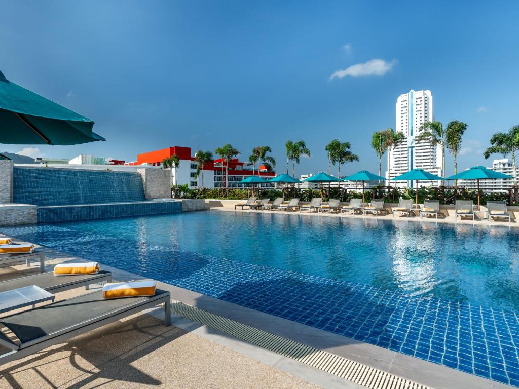 a large swimming pool with chairs and blue umbrellas at M Social Hotel Phuket in Patong Beach
