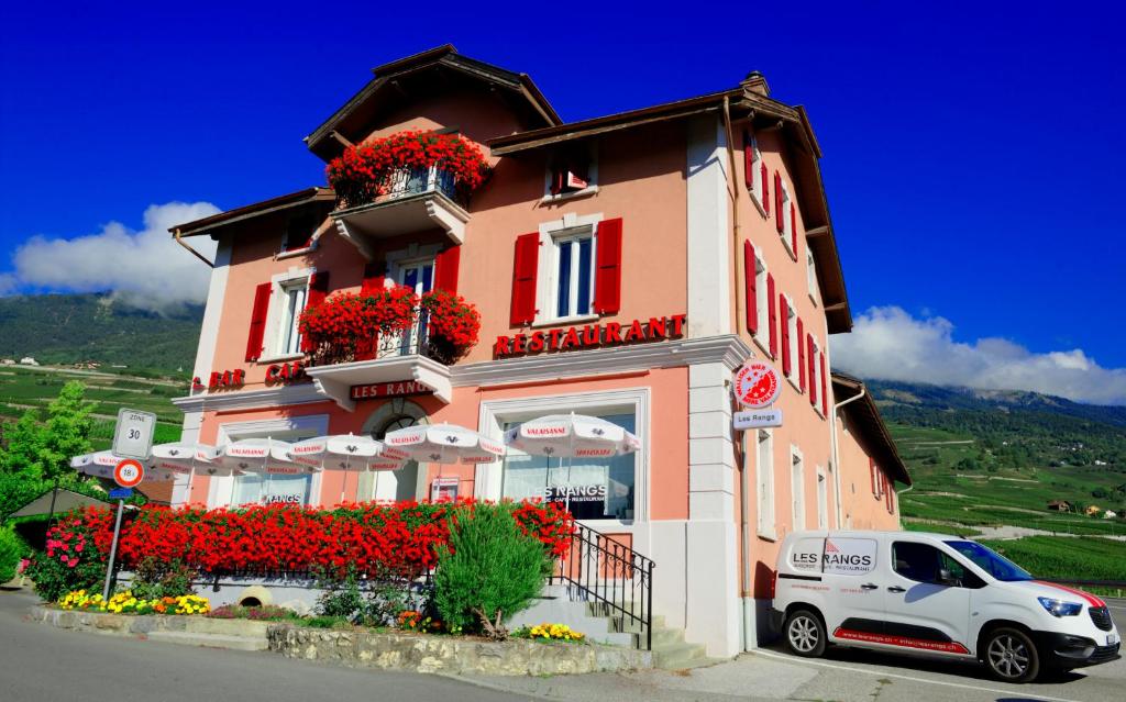a building with flowers and a white car parked in front at Auberge Les Rangs in Conthey