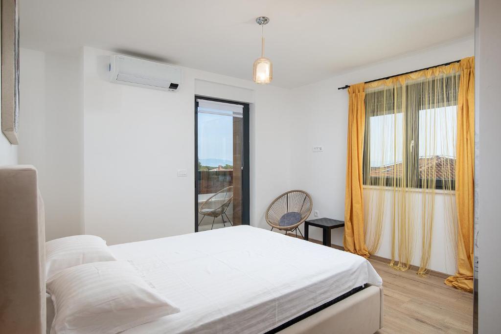 a white bedroom with a bed and a window at Apartments Sara II in Ližnjan