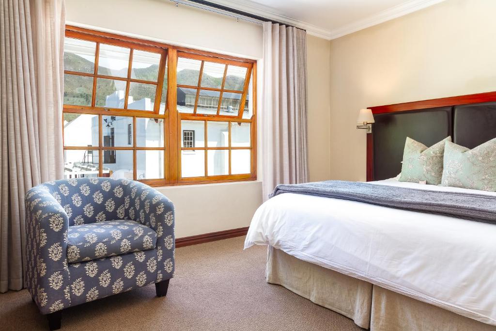 a bedroom with a bed and a chair and a window at Noordhoek Village Hotel in Noordhoek