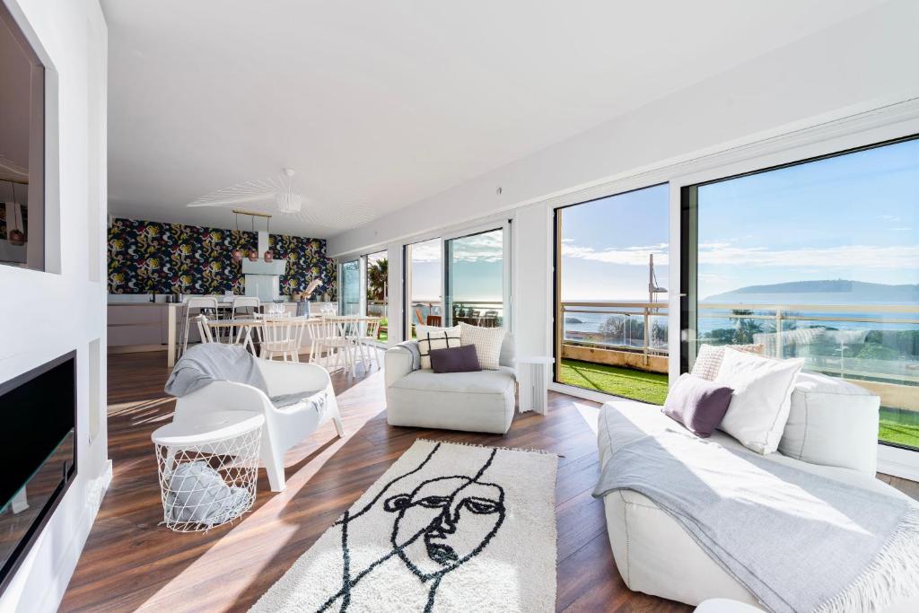 Elle comprend un salon doté d'un mobilier blanc et de grandes fenêtres. dans l'établissement Grand Appartement Balcon Vue Mer 20m Plage Mourillon, à Toulon
