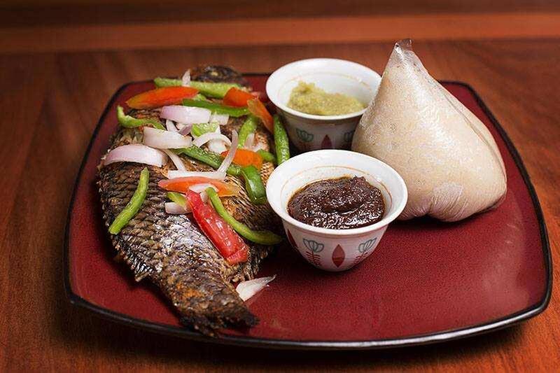 a plate of food with fish and vegetables and dipping sauces at Etna Apartments in Takoradi