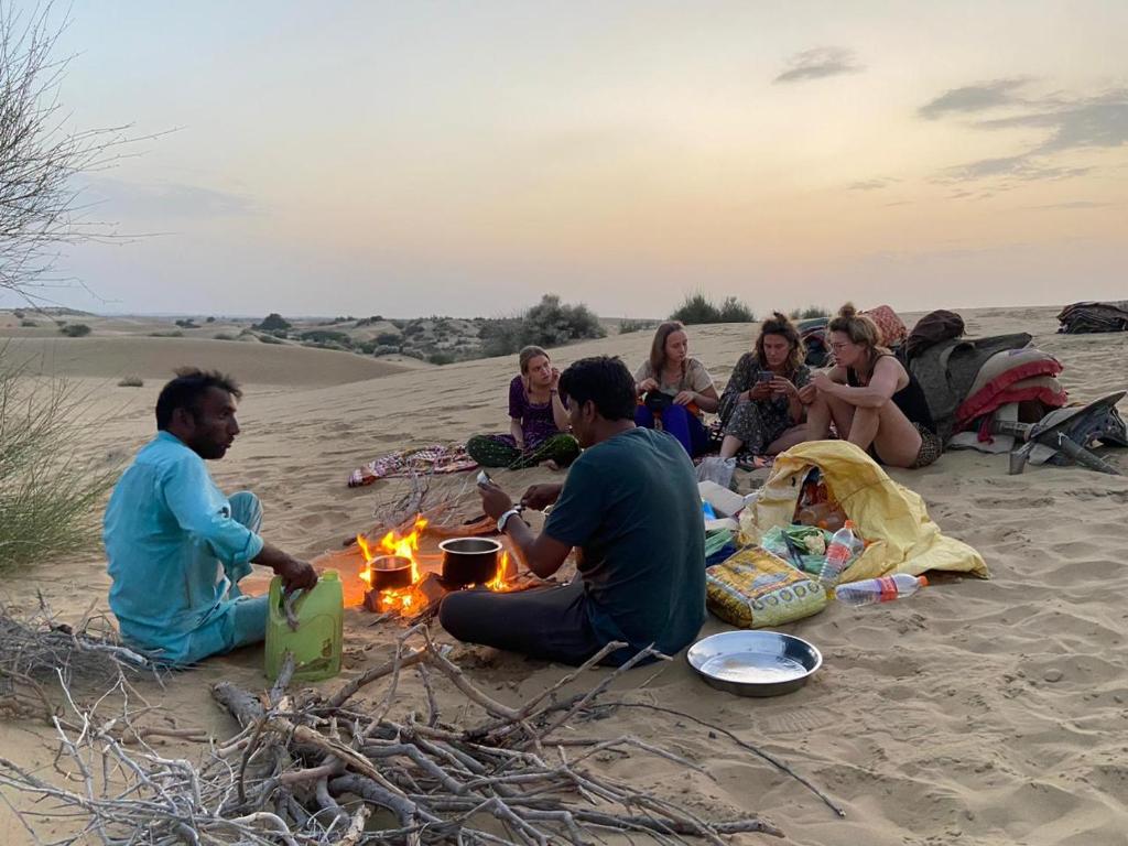 a group of people sitting around a fire in the sand at Little Prince Home Stay in Jaisalmer