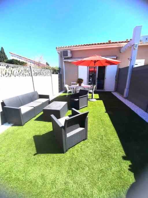 d'une terrasse avec deux canapés et un parasol rouge. dans l'établissement Jolie maisonnette, à Palavas-les-Flots