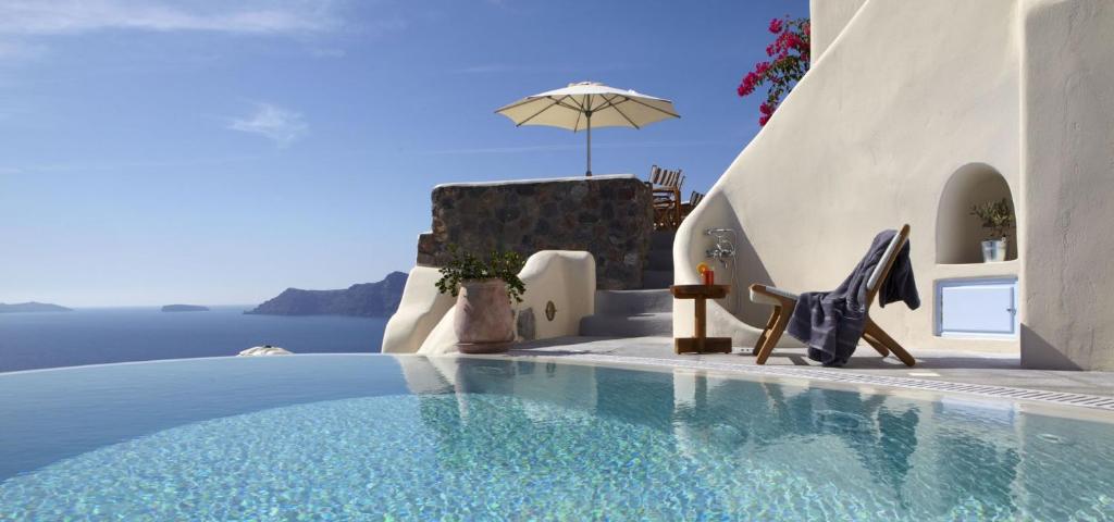 a swimming pool with a chair and an umbrella at Pezoules of Oia in Oia