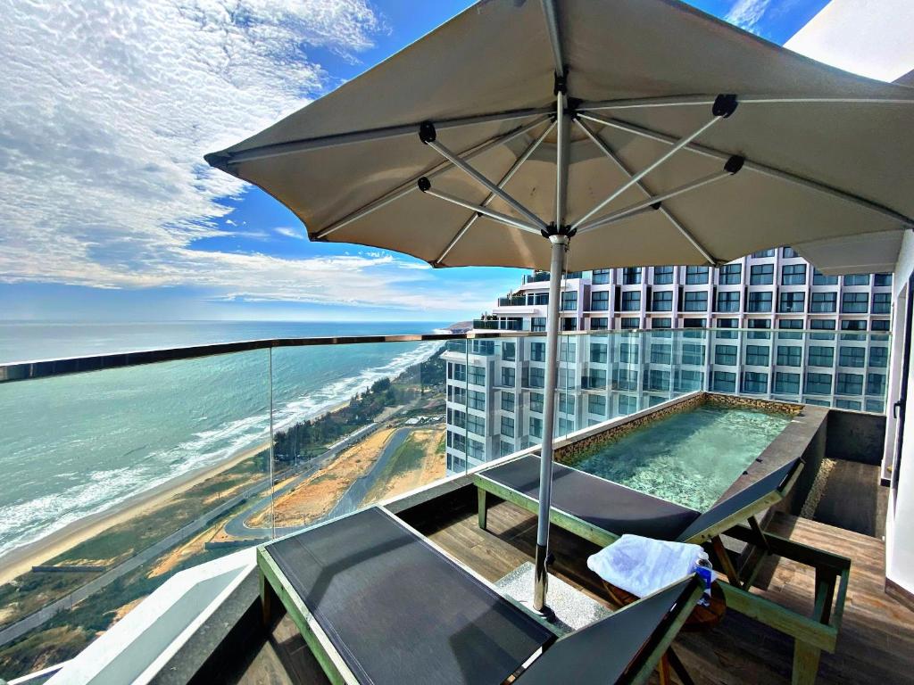 een zwembad met een parasol op een balkon met een gebouw bij Apec Mandala Mũi Né - Khách Sạn Nghĩ Dưỡng Luxury Limited in Ấp Thiẹn Ái