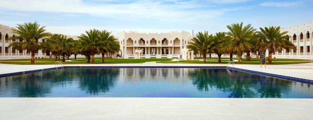 a swimming pool in front of a building with palm trees at Liwa Hotel in Mezairaa
