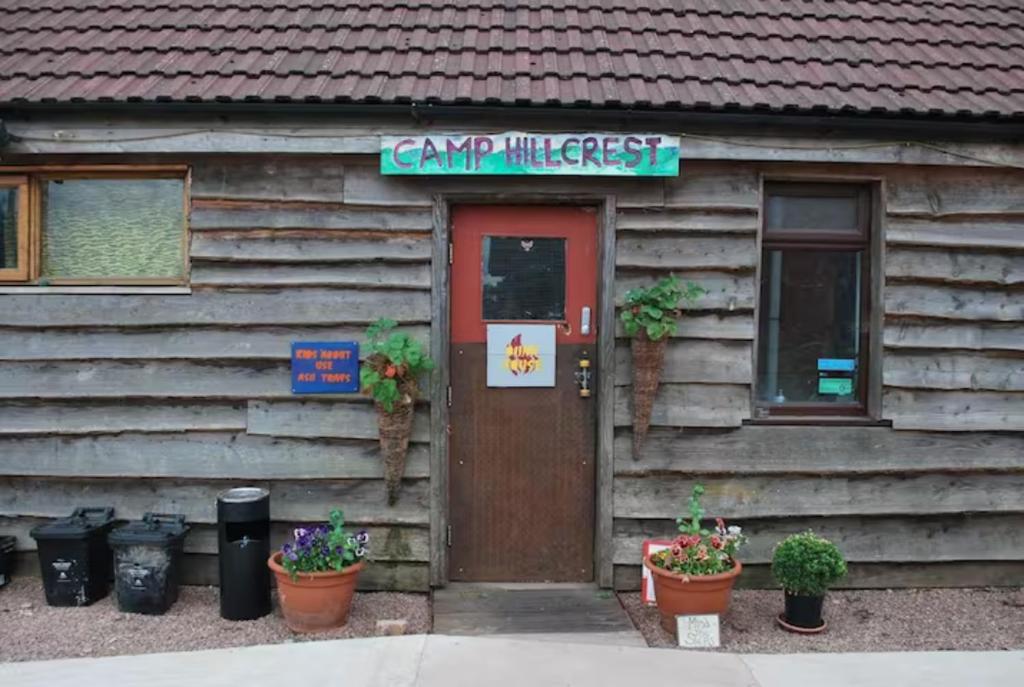 a cabin with a sign on the door and plants at Camp Hillcrest Bunkhouse 