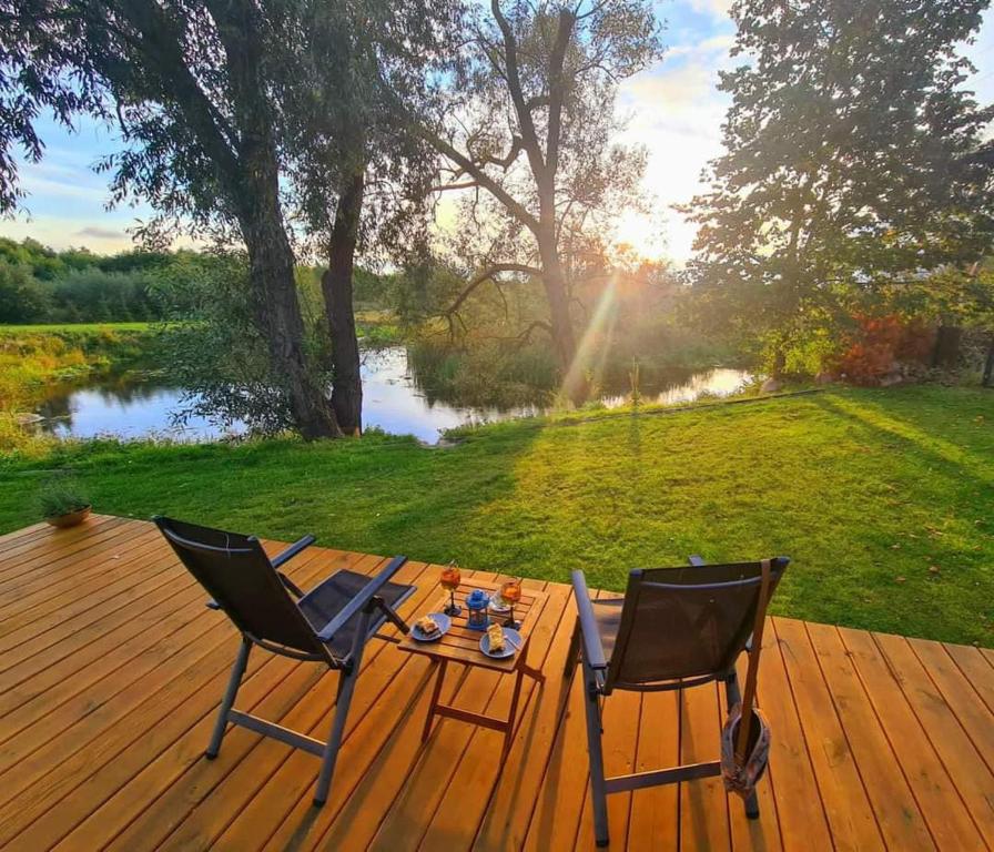 two chairs and a table on a wooden deck with a lake at Heaven Reset & Spa - Domek przy lesie in Korczew