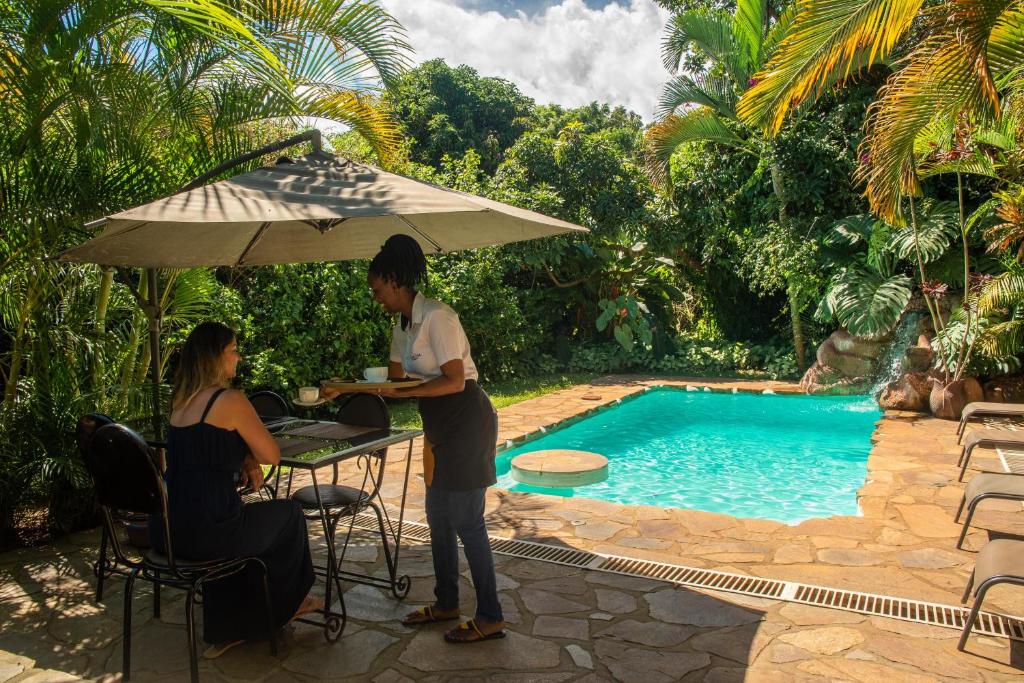 un hombre y una mujer sentados en una mesa junto a una piscina en Karibu Entebbe, en Entebbe