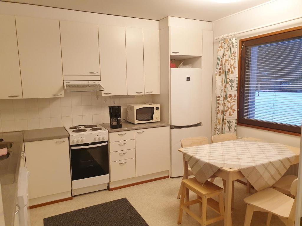 cocina con armarios blancos, mesa y microondas en Saunallinen rivitalohuoneisto A1 59m2, en Säviä