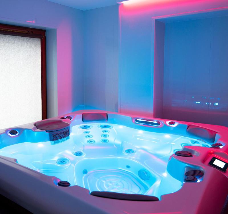 a hot tub in a room with blue and pink at Jacuzzi City Kraków in Kraków
