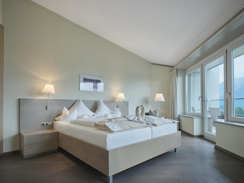 a white bedroom with a large bed and large windows at Park Igls - Medical Spa Resort in Innsbruck