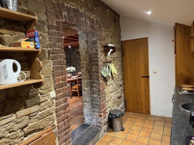a kitchen with a stone wall with a door and a table at Gîte Le fournil in Modave