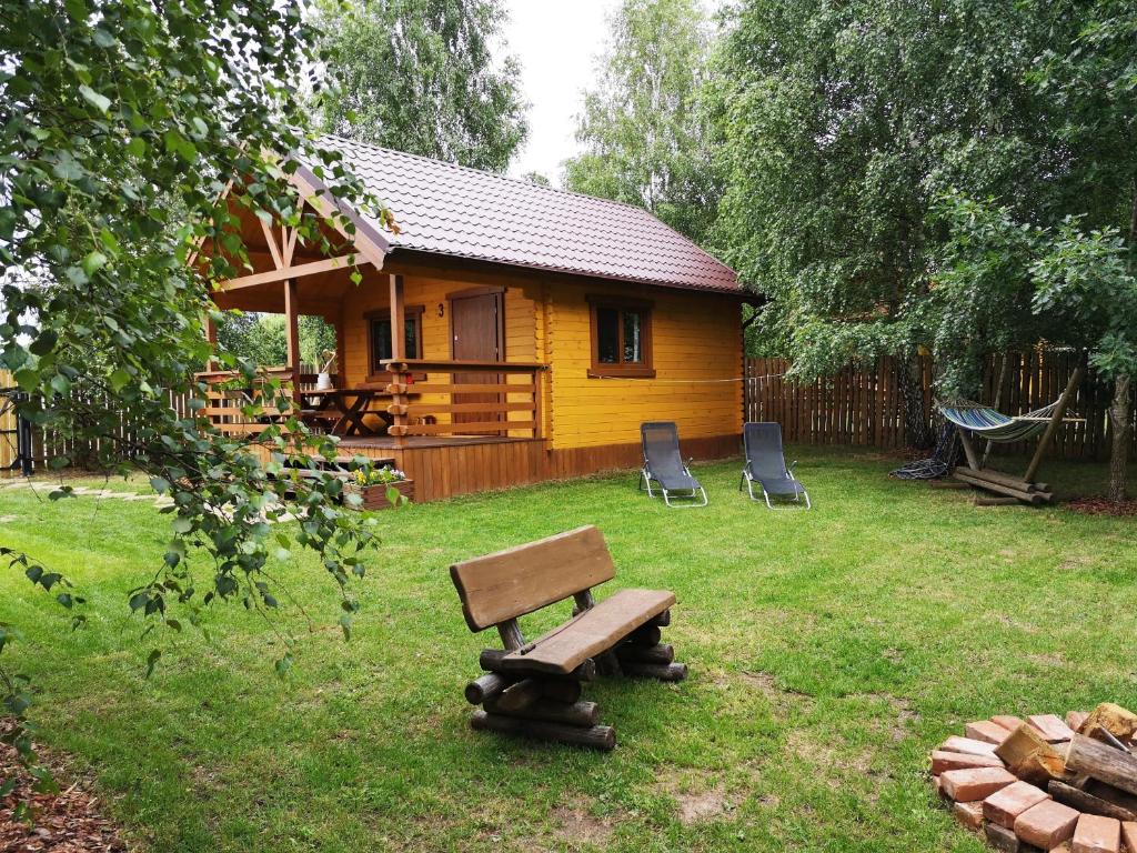 una cabaña amarilla con 2 sillas y un banco en un patio en Wielewski Zakątek, en Wiele