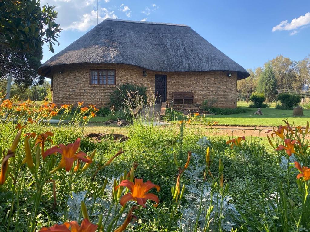 a building with a thatched roof with a field of flowers at Soetgeluk Farm Cottage in Hekpoort