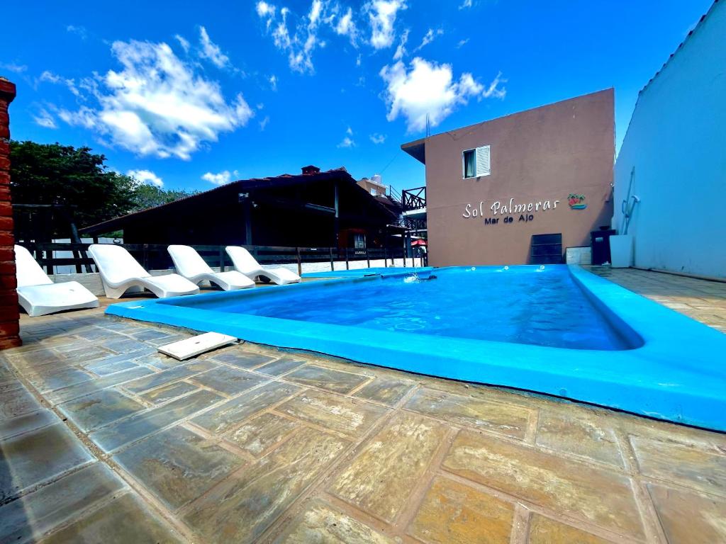 a swimming pool with chairs and a building at Complejo Sol Palmeras in Mar de Ajó