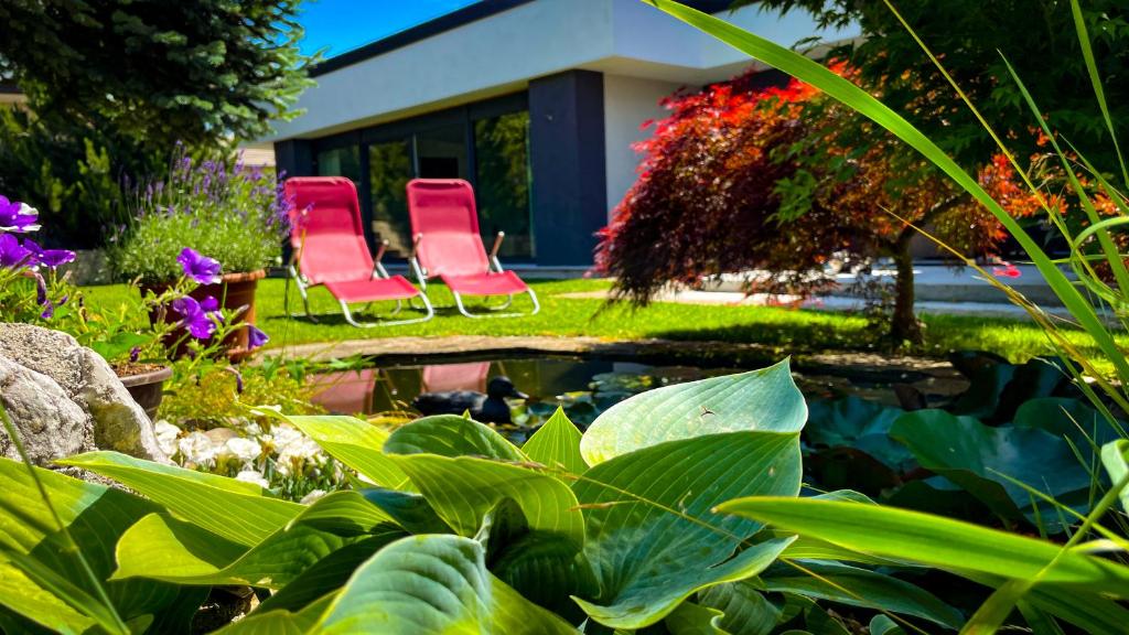 2 chaises rouges assises à côté d'un étang dans un jardin dans l'établissement Green Oasis Garden, à Šenčur