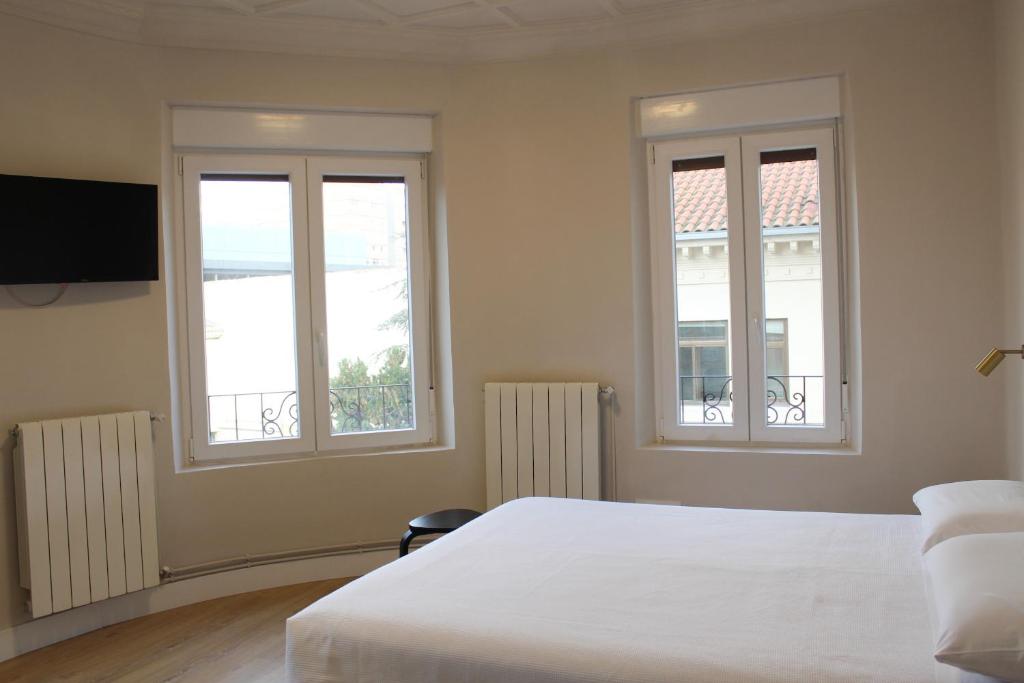 a bedroom with two windows and a white bed at Monasterio Centro Histórico in Burgos