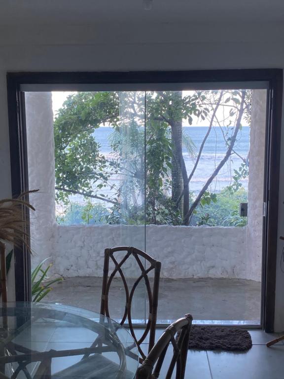 une table et des chaises en verre dans une chambre avec une grande fenêtre dans l'établissement Casa beira do mar, à Florianópolis