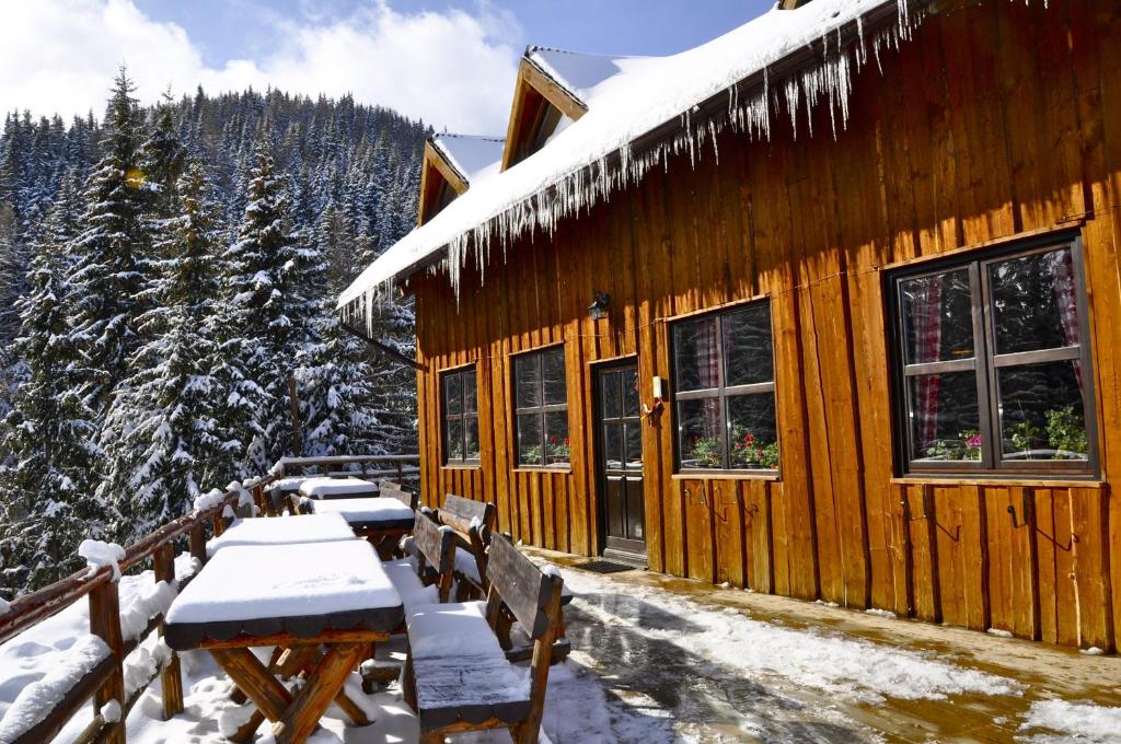 Cabaña de madera con nieve en las ventanas y mesas en Cabana Stana Tarle en Sinaia