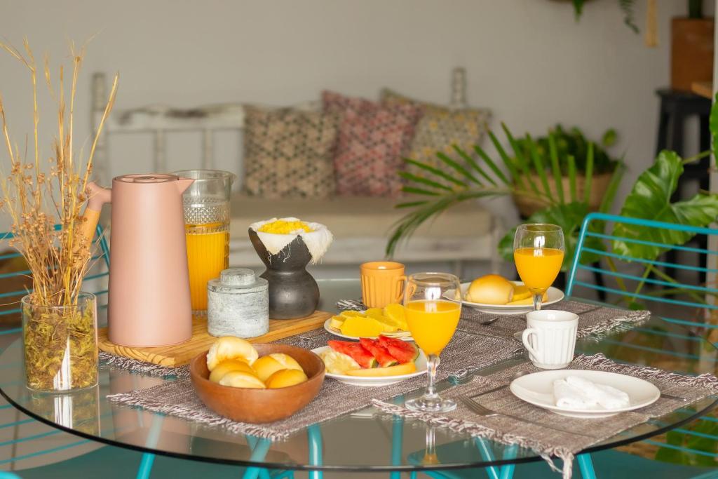 une table en verre avec de la nourriture, des oranges et des verres de jus d'orange dans l'établissement Refúgio Urbano, à Campina Grande