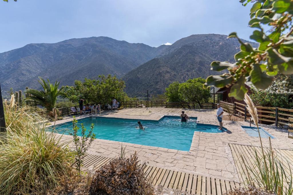 a pool with people in it with mountains in the background at Las lomitas de Guayacan, Cabañas y Spa in San José de Maipo