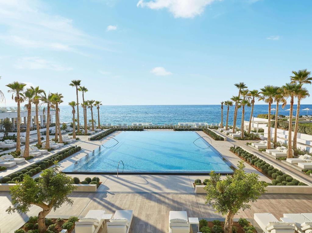 uma vista sobre uma piscina com palmeiras e o oceano em Grecotel LUX.ME White Palace​ em Adelianos Kampos