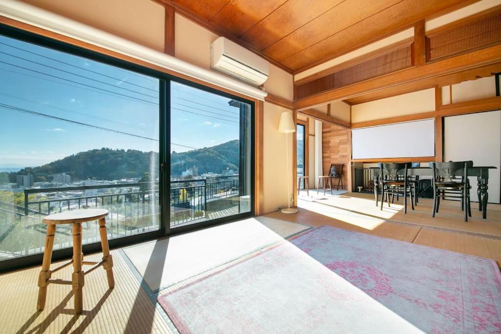 Zimmer mit einem großen Fenster mit einem Tisch und Stühlen in der Unterkunft 湯河原「ゲストハウス城堀の家」 in Yugawara