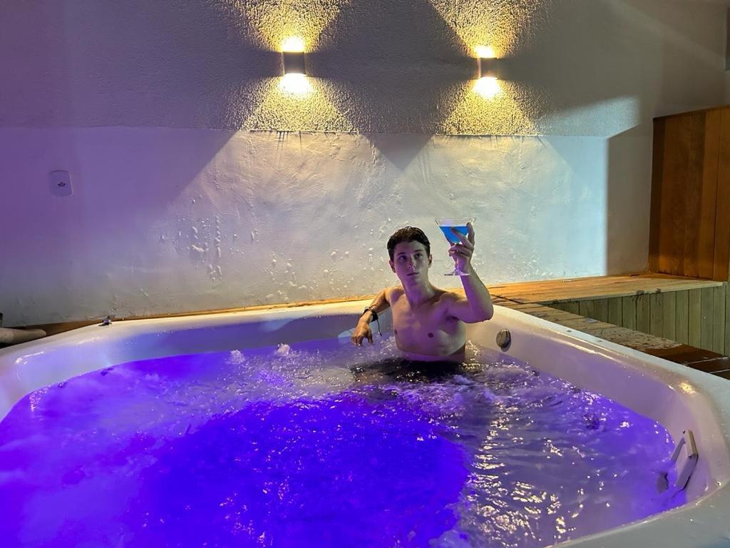 Ein Mann in einer Badewanne voller lila Wasser. in der Unterkunft Pousada Velas do Forte in Cabo Frio