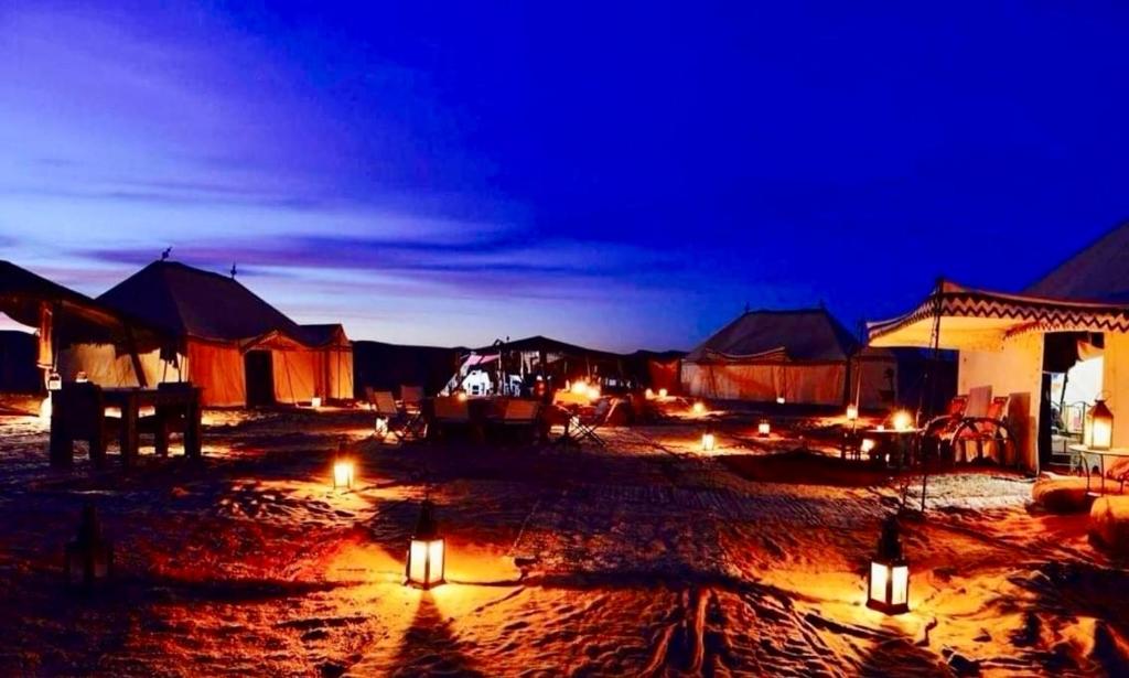 a group of tents with lights in the sand at night at Berber & Camel Trek in Merzouga