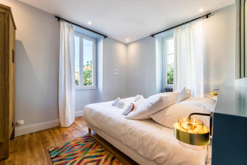 a bedroom with a bed with white pillows and windows at ALOE KEYWEEK Architect Apartment with terrace and garage Biarritz in Biarritz