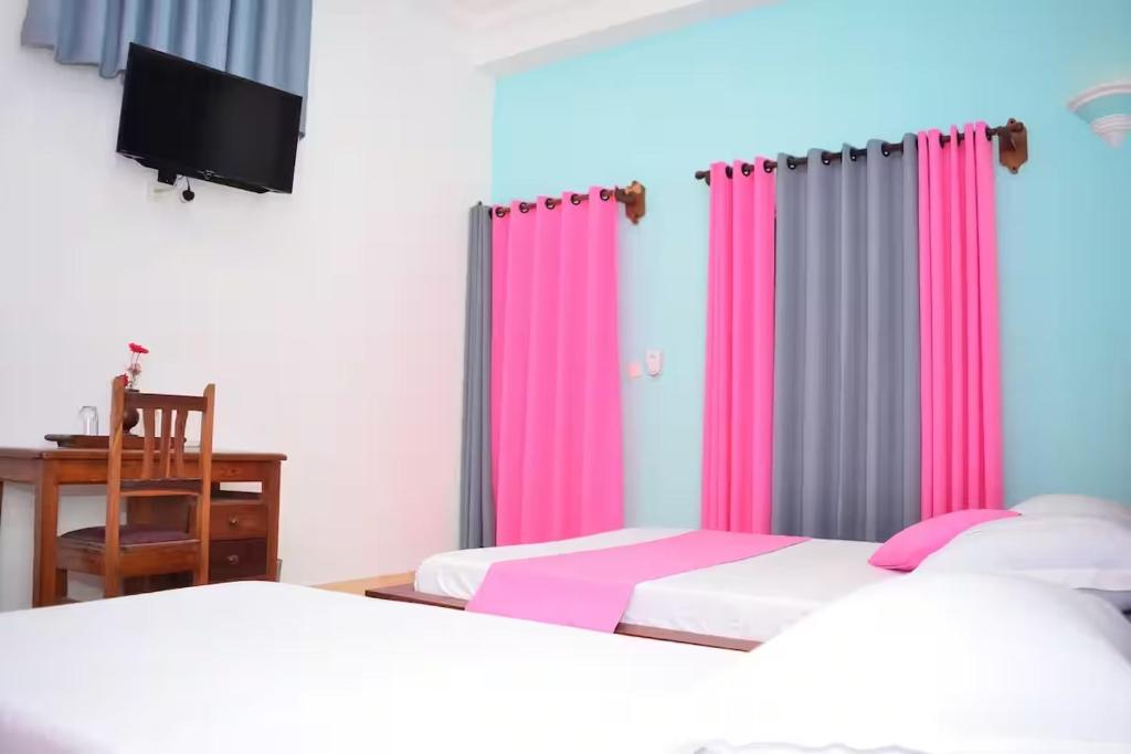 two beds in a room with pink and gray curtains at HOTEL AKBAR in Mahajanga
