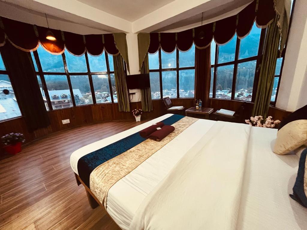 ein großes Schlafzimmer mit einem großen Bett und großen Fenstern in der Unterkunft Hotel Sky Mountain View by Hadimba Palace - Manali in Manali